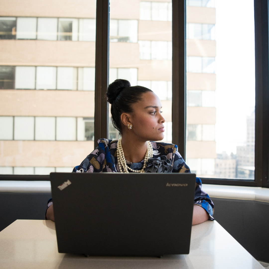 woman sitting at a table with a computer on a desk looks away